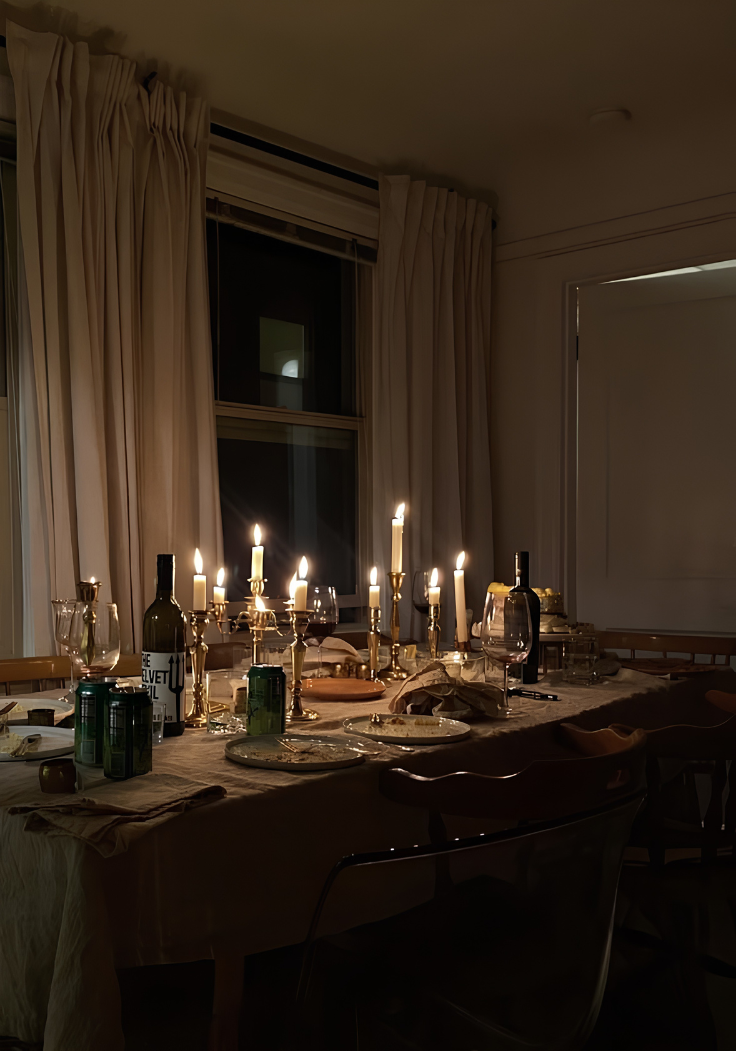 A long table set with candles, wine and linen in a warm, dimly lit dining room
